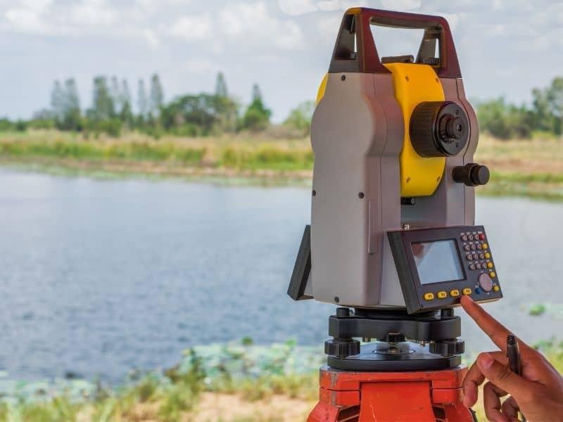 Survey instrument positioned near a waterfront property where land surveying supports future utility improvements